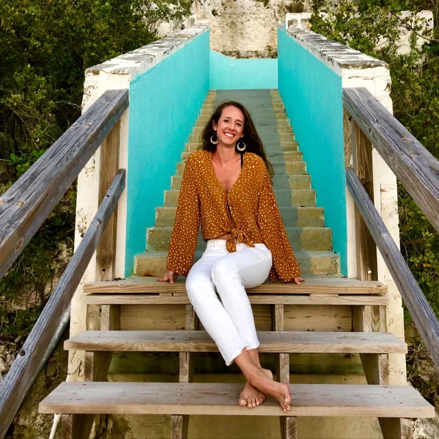 Stacy Sivco wearing a tan top and white pants in front of a turquoise staircase outside