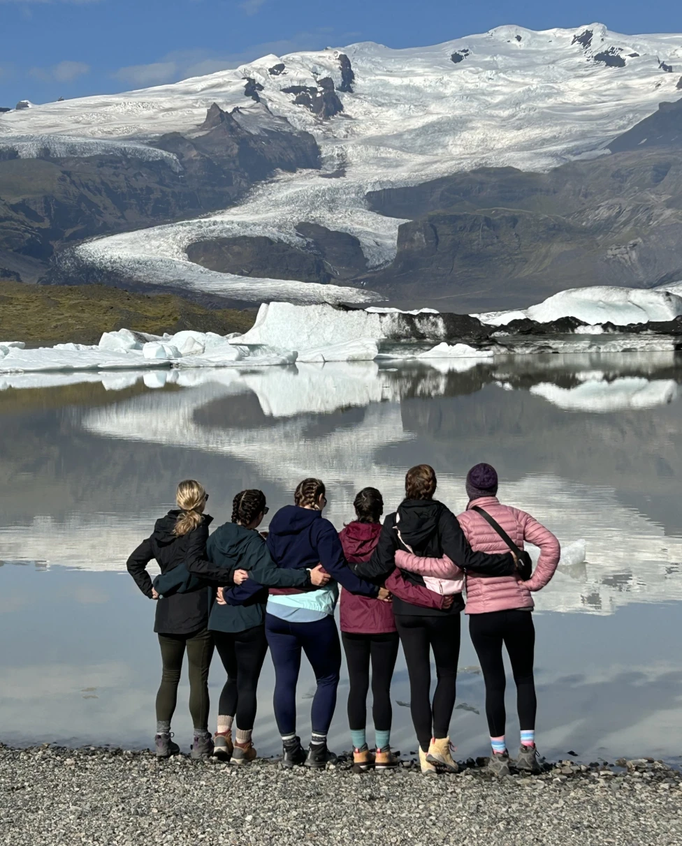 6 girls facing a lake with snow covered mountains.
