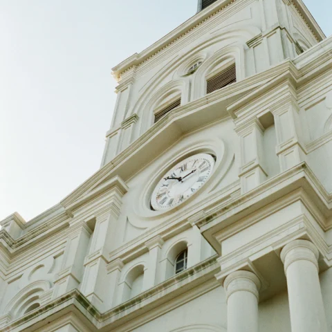 A low-angled shot of a white-colored building with a clock in the middle located close to the Mercantile Hotel, New Orleans
