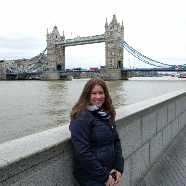 Travel Advisor Hilary Gwaltney in a blue jacket standing in front of the Tower Bridge in London.