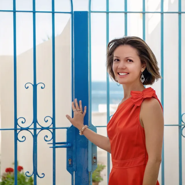 Travel Advisor Amalia Maloney wears an orange dress in front of a blue gate