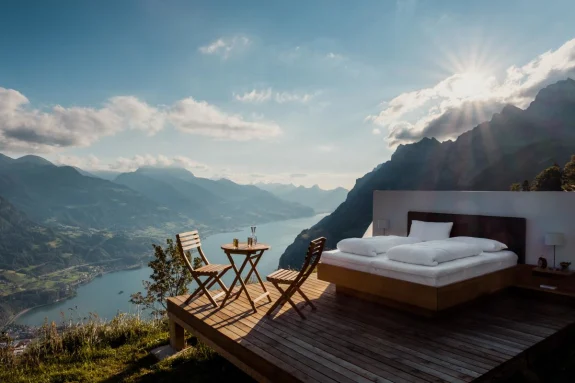 Outdoor room accommodation at boutique resort with bed and patio table that overlooks a canal and mountain valleys in Walensee, Switzerland.