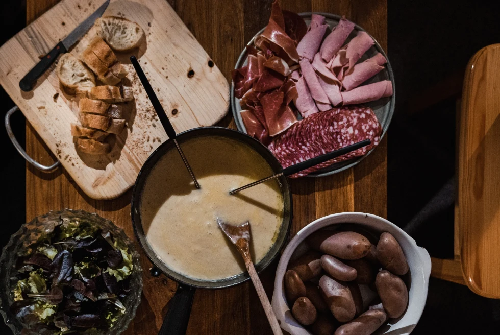 Boiling pot of Switzerland with charcuterie, vegetables, potatoes and bread on the side on wooden table.