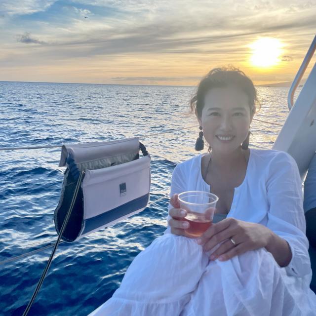 Jini Cho wearing white dress and holding drink in front of the sunset