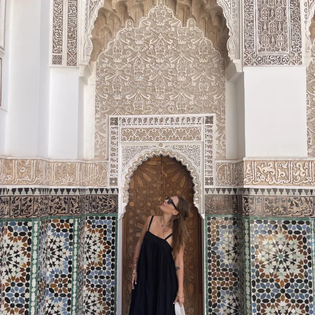 Travel Advisor Lana True stands in an entry way of a wooden door of an ornate tiled wall wearing a black dress and sunglasses
