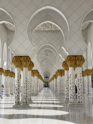 A white and gold mosque with several rows of arches and pillars in the UAE.