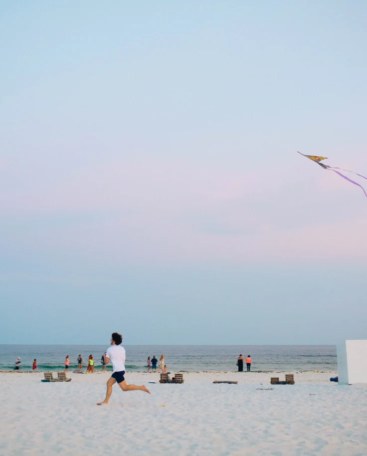 Kid running on the beach with a kite and a pastel sunset in the background