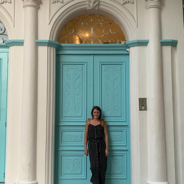 Fora travel agent Caitlyn Johnston stands in front of turquoise door and white archway