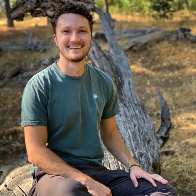 Travel advisor Greyson Kountz smiling and sitting on a wood.