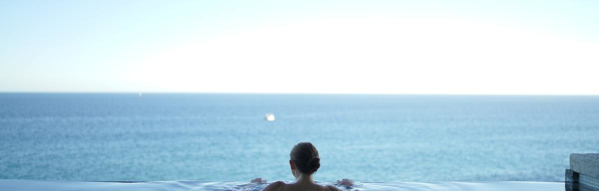 Woman relaxing in infinity pool overlooking the ocean on a bright day.