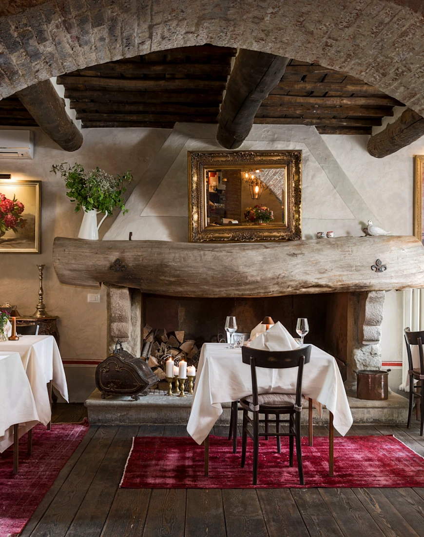 tables with white tablecloths sit on red rugs beneath a large brick archway