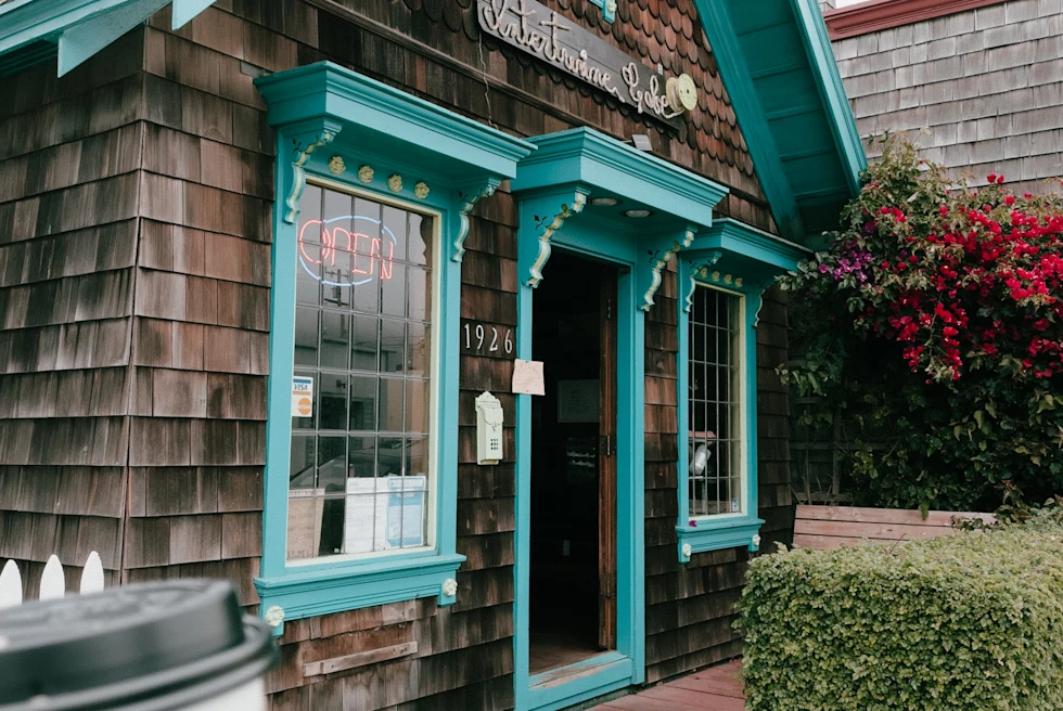 Person holding cup of coffee in front of building made out of driftwood with blue paint during daytime