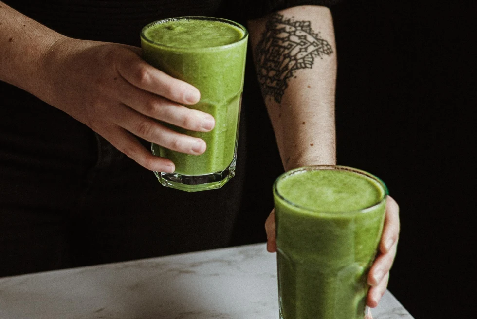 person with mandala tattoo holding two green juice in clear glasses