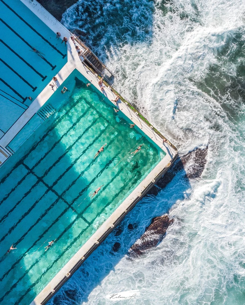 aerial view of people swimming in a pool near the ocean