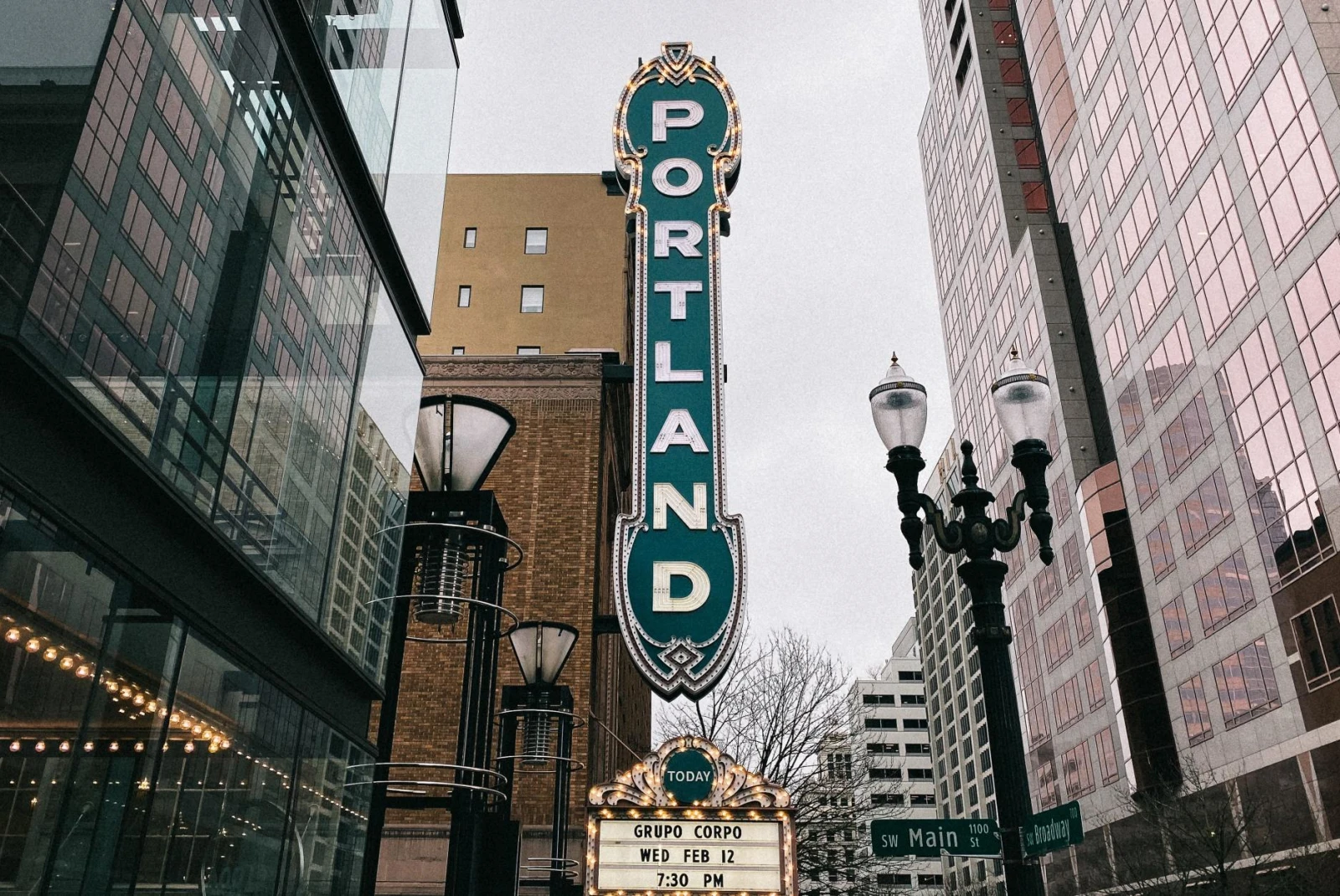 long old school vertical sign over a theater reads, "portland" in white letters, surrounded by large glass high rise buildings 