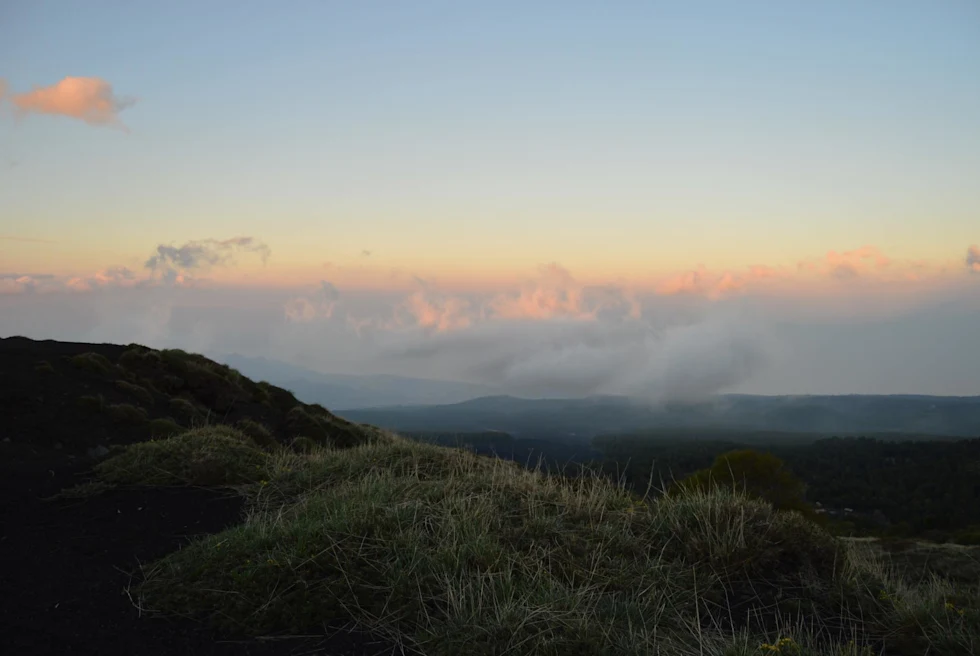 rolling hills at sunset with a volcano in the distant mountain range surrounded by clouds and smoke