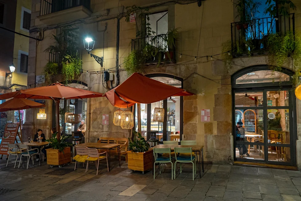 outside of a restaurant at night with umbrellas over table and chairs on an old city street