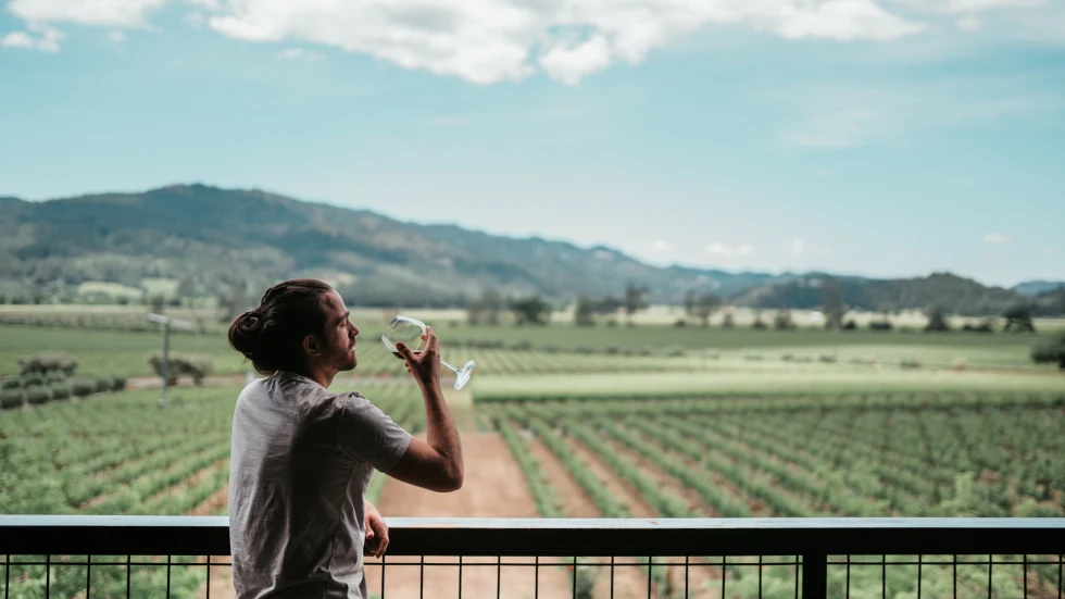 man holding wine glass standing on patio overlooking vineyards