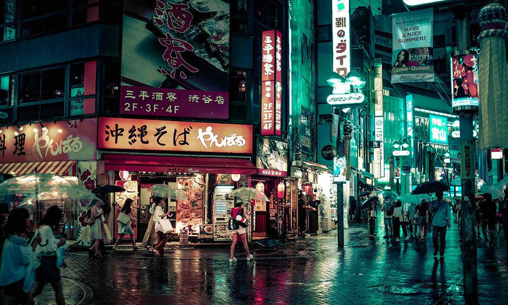 Nighttime in Japan city street raining umbrellas people walking 