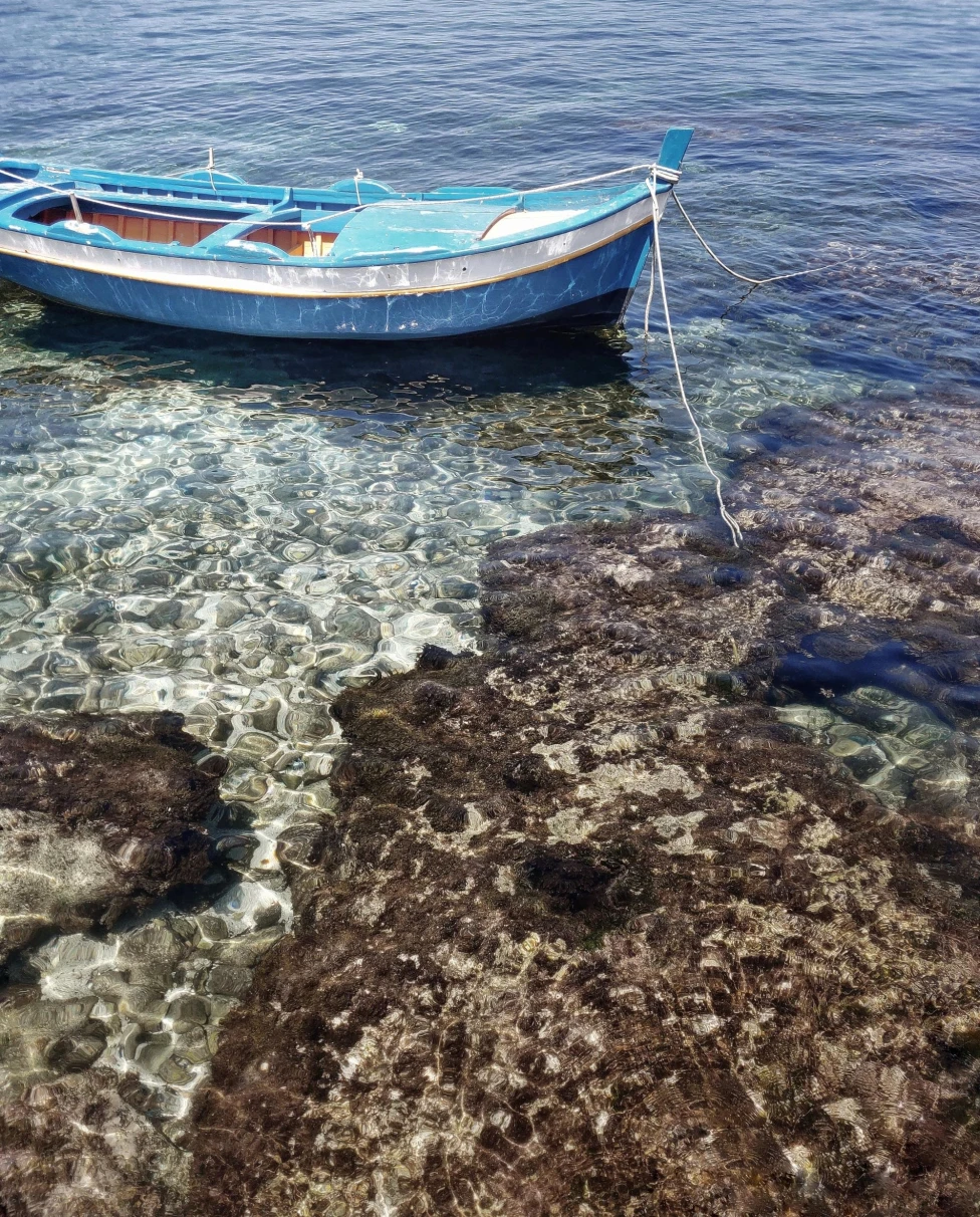 a blue row boat is tied to the shallow rocks in clear blue water 
