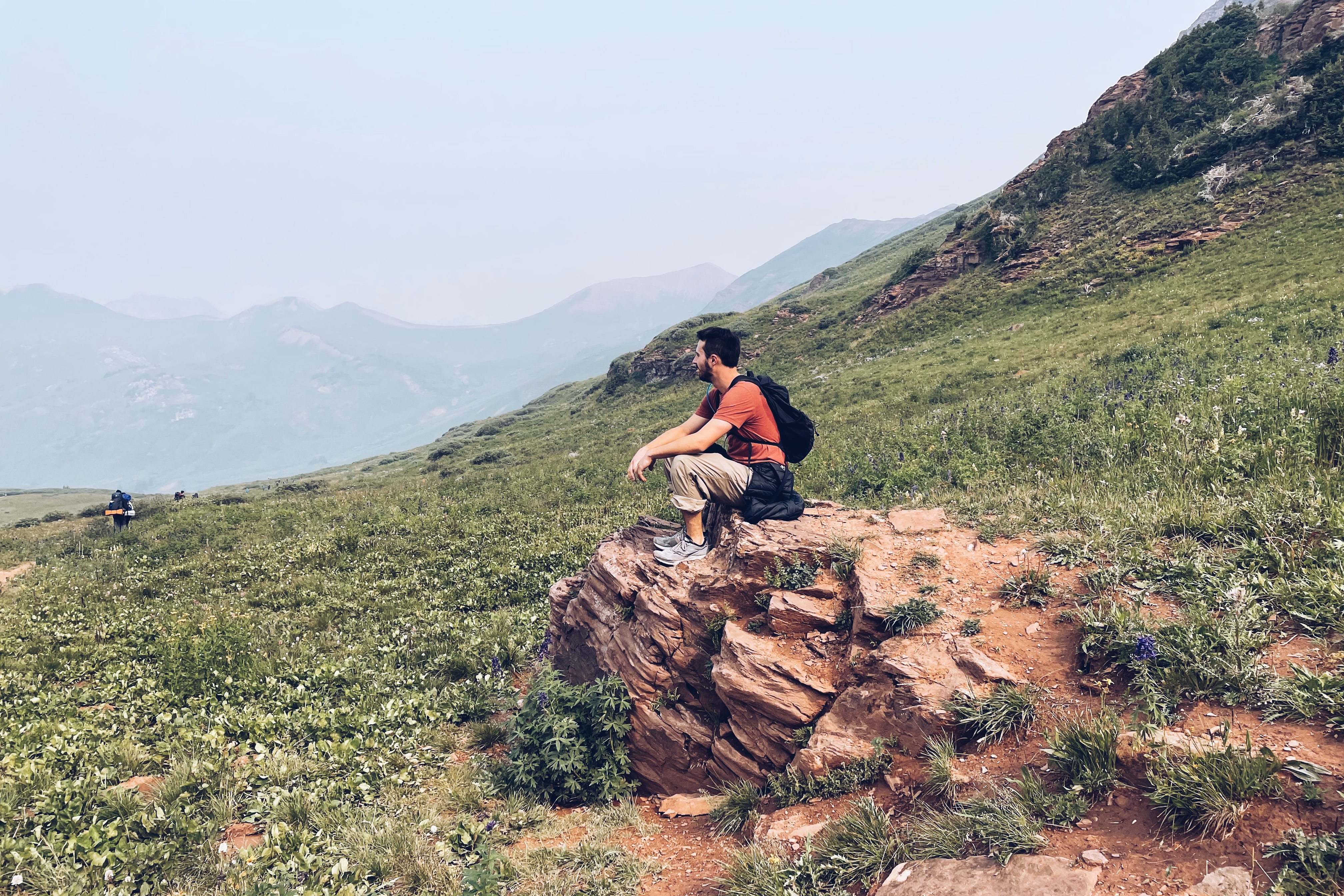 A man sitting on the rock watching the green hills. 