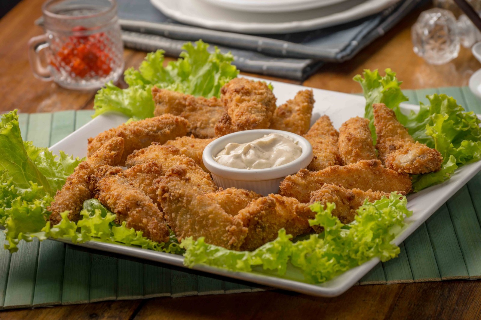 Tan chicken fingers with green lettuce on a white plate and white sauce in the center in Madeira, Portugal.