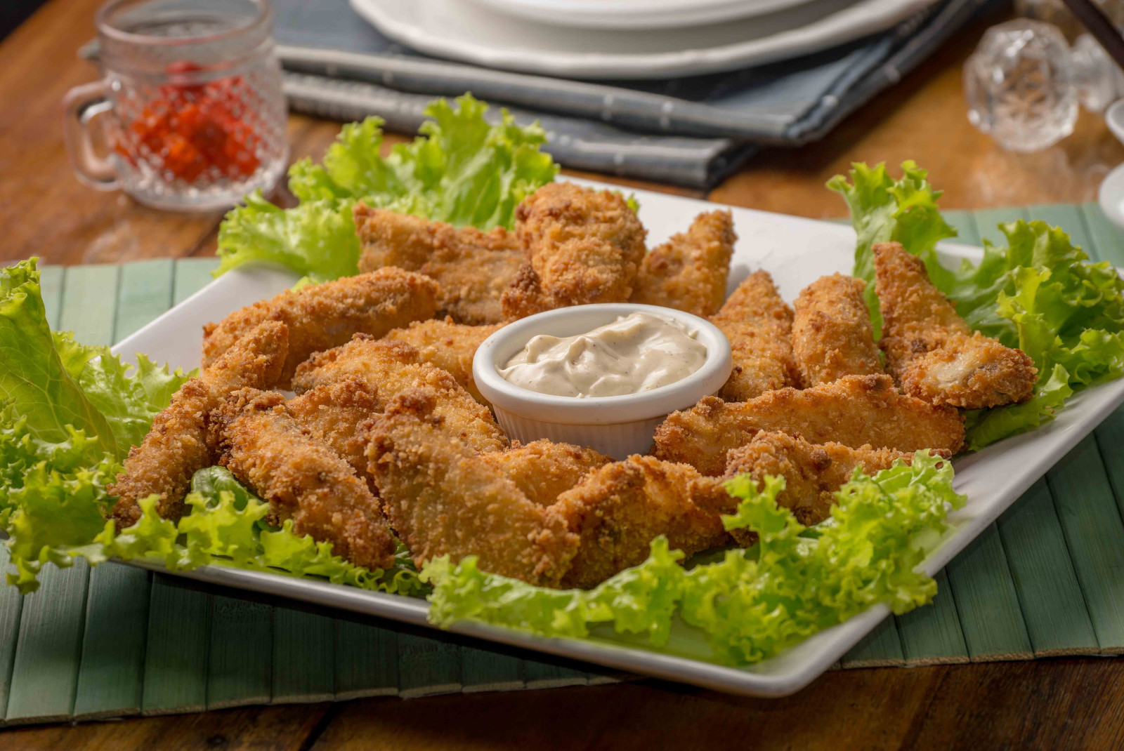 Tan chicken fingers with green lettuce on a white plate and white sauce in the center in Madeira, Portugal.