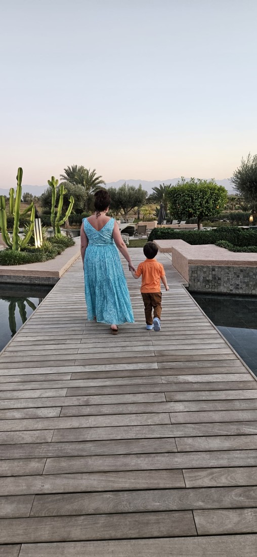 A woman in a blue dress holding the hand of a small child as they walk down a wooden walkway 