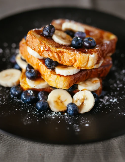 French toast with blueberries and bananas on black plate