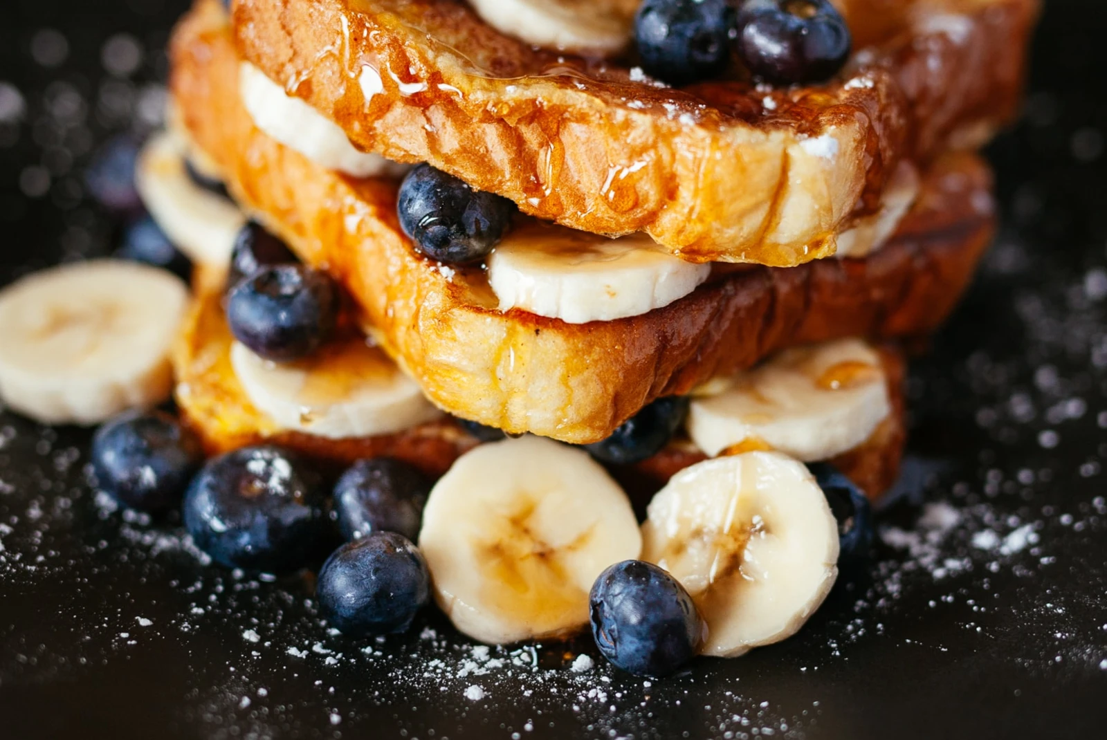 French toast with blueberries and bananas on black plate