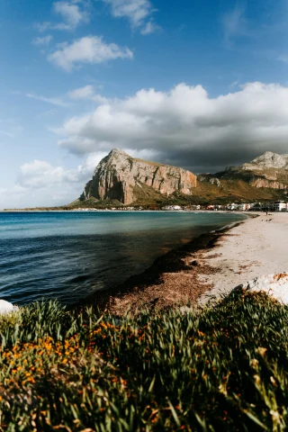 The image showcases a picturesque coastal scene with a mountain backdrop and a beachfront, adorned with local flora.