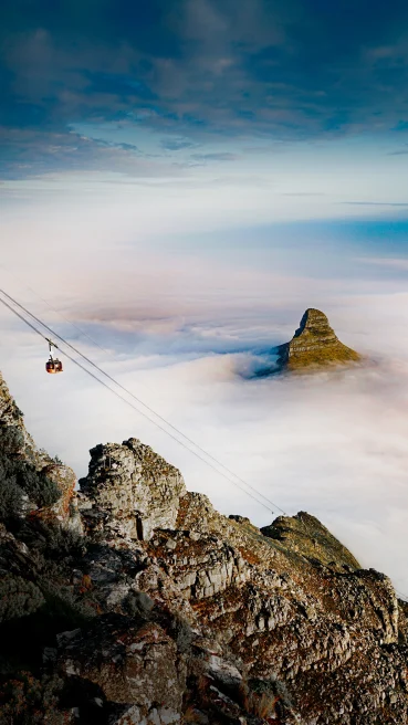 an ascending cablecar and mountain peak emerging through a blanket of clouds