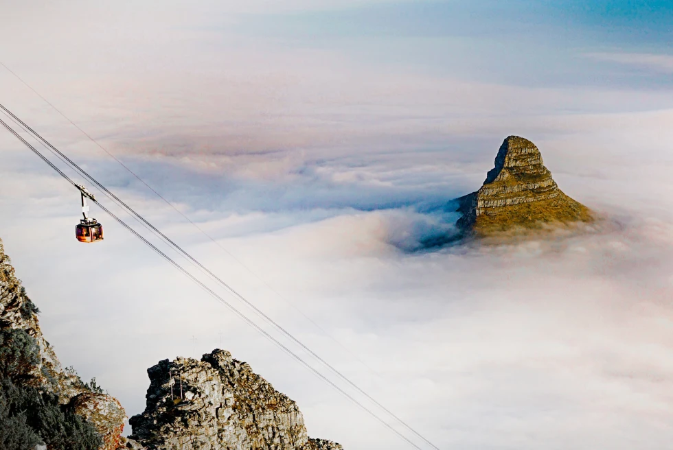 an ascending cablecar and mountain peak emerging through a blanket of clouds