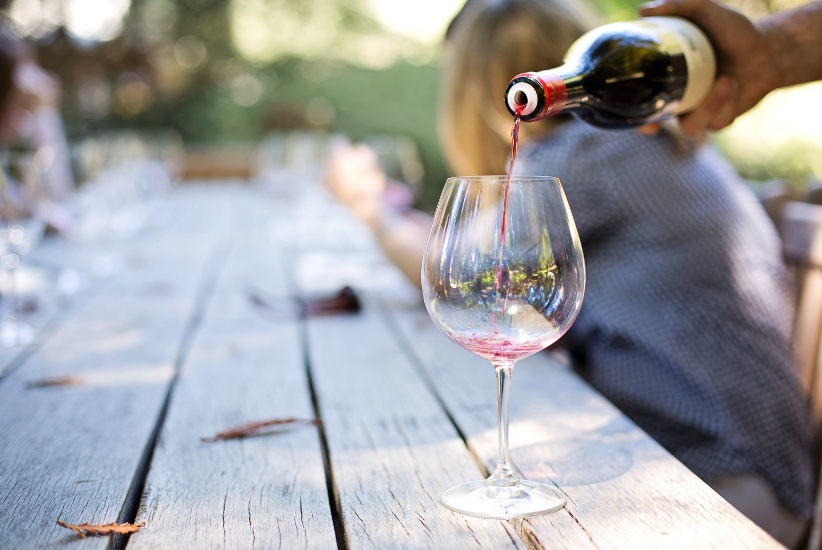 Red wine being poured into wine glass with person sitting in background