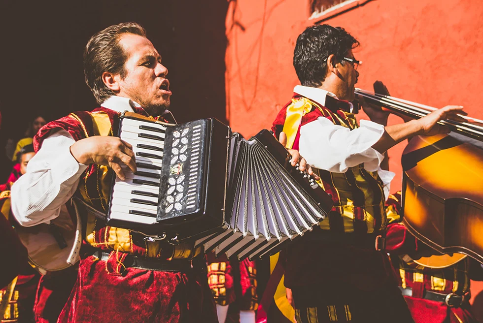 San Miguel de Allende Mexico street performers two men playing musical instruments with red yellow and white traditional clothing and a red orange wall behind them