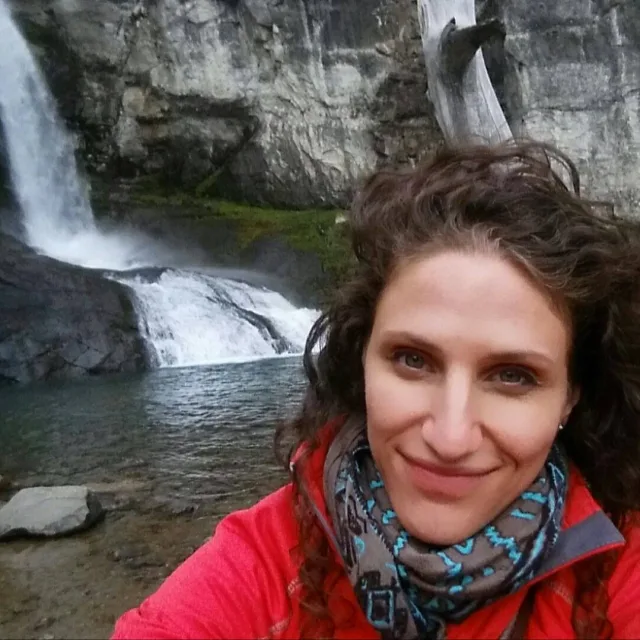Travel Advisor Allison King with a red jacket and a waterfall behind.