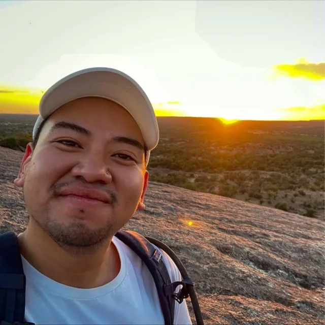 Travel Advisor James Vongprachanh with a white shirt and hat and a sunset in the distance.
