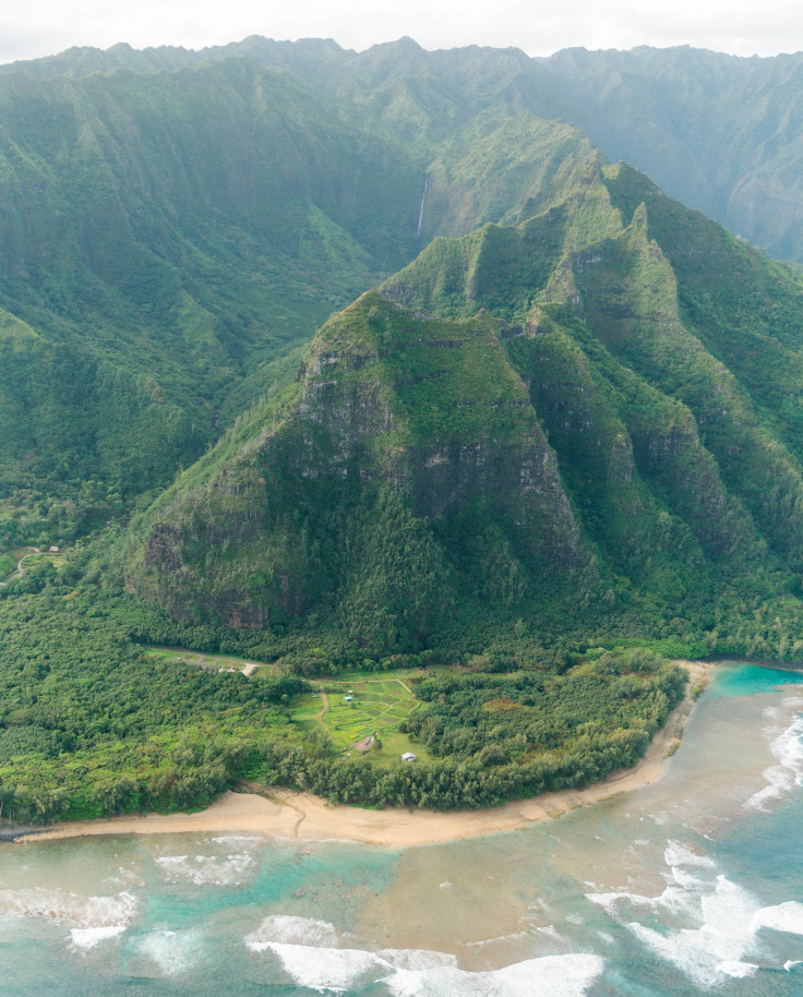 Aerial view of green mountains next to sandy beach and body of water during daytime