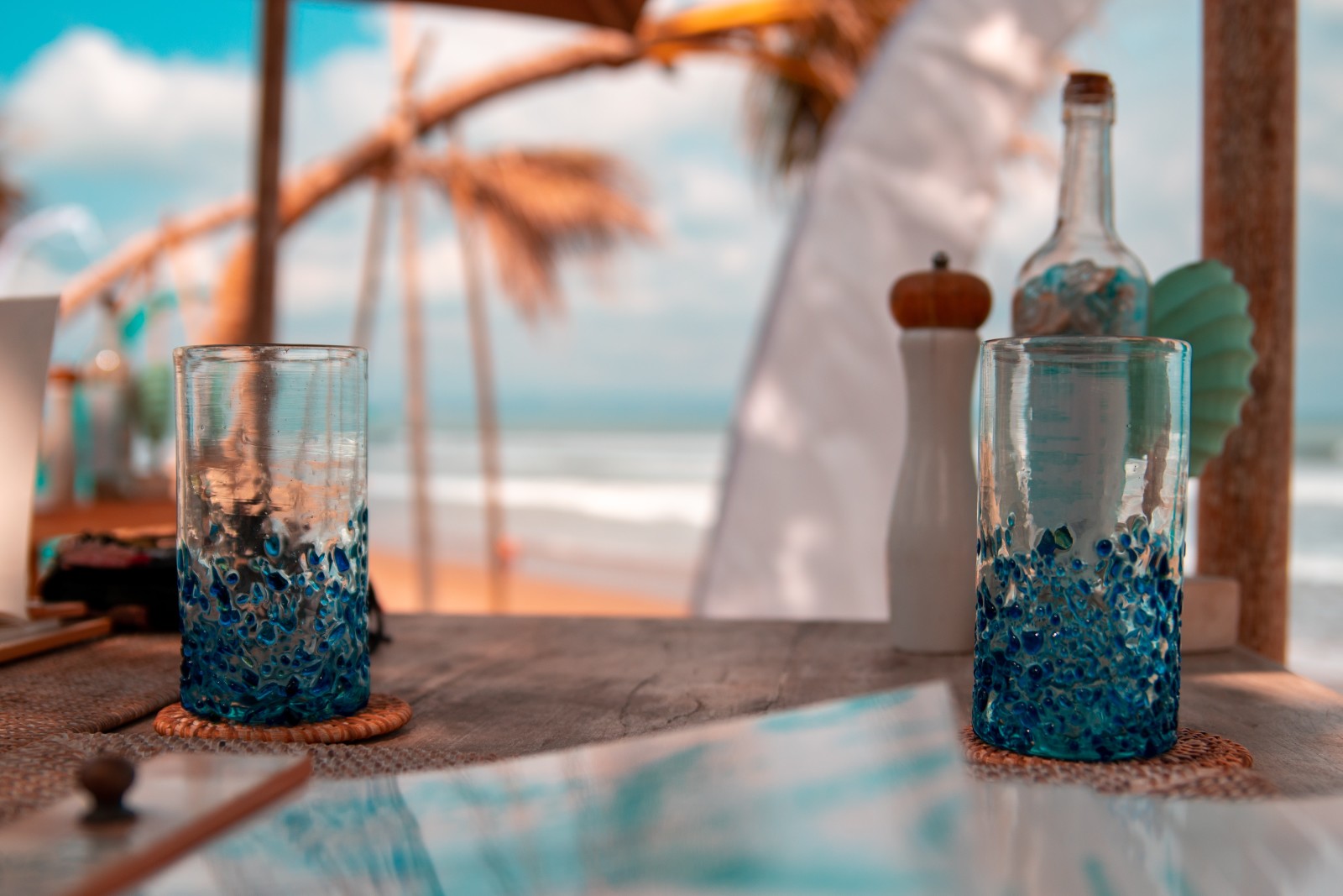Two glasses on wooden table with beach in background during daytime