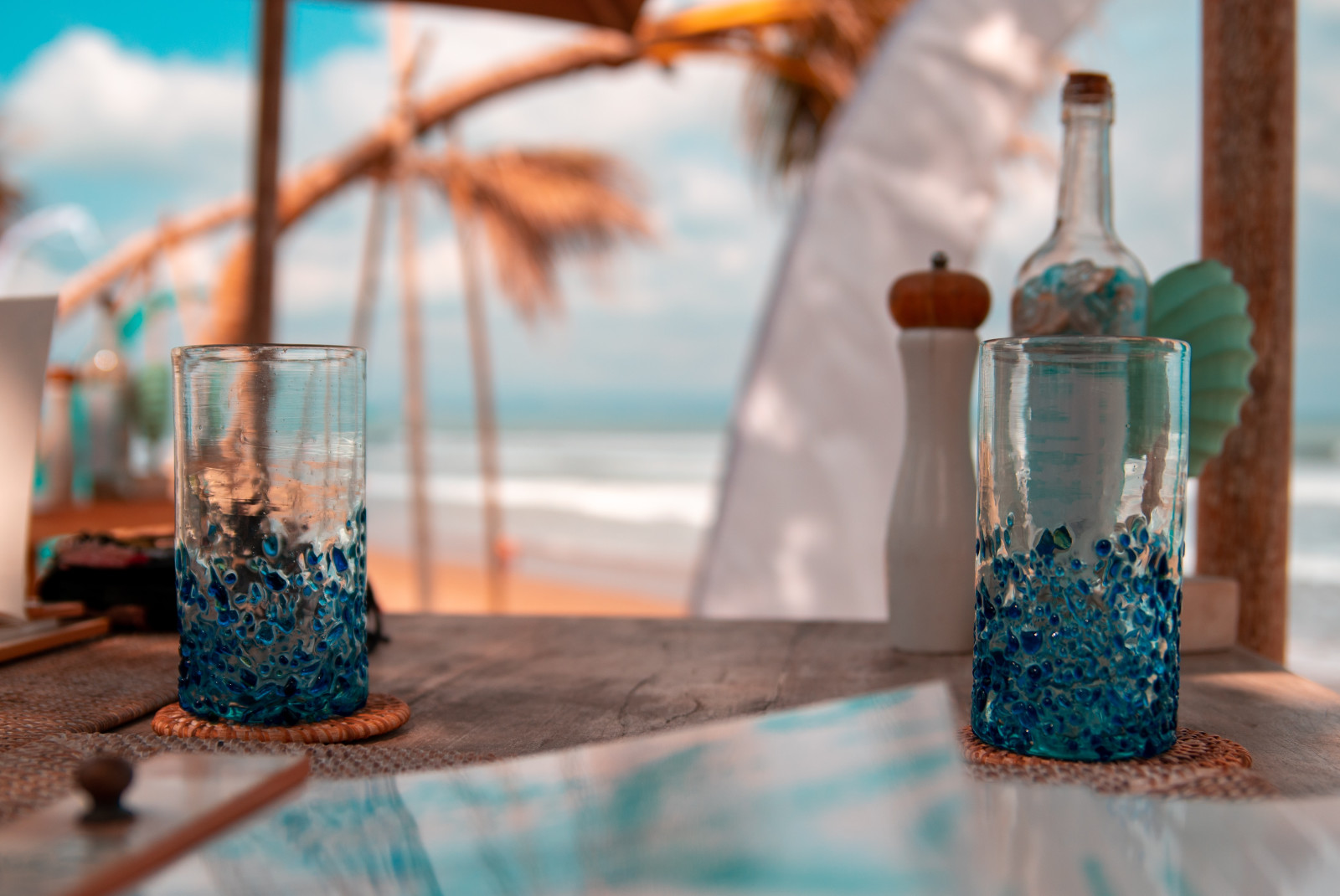 Two glasses on wooden table with beach in background during daytime