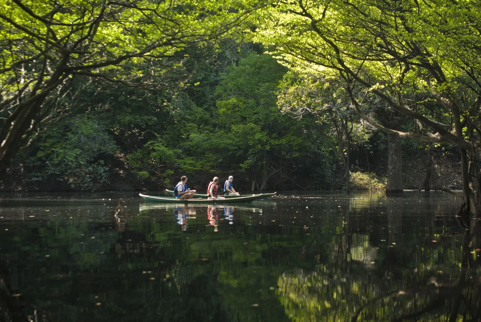 a three person kayak on a pristine river surrounded by lush trees reflected in the water