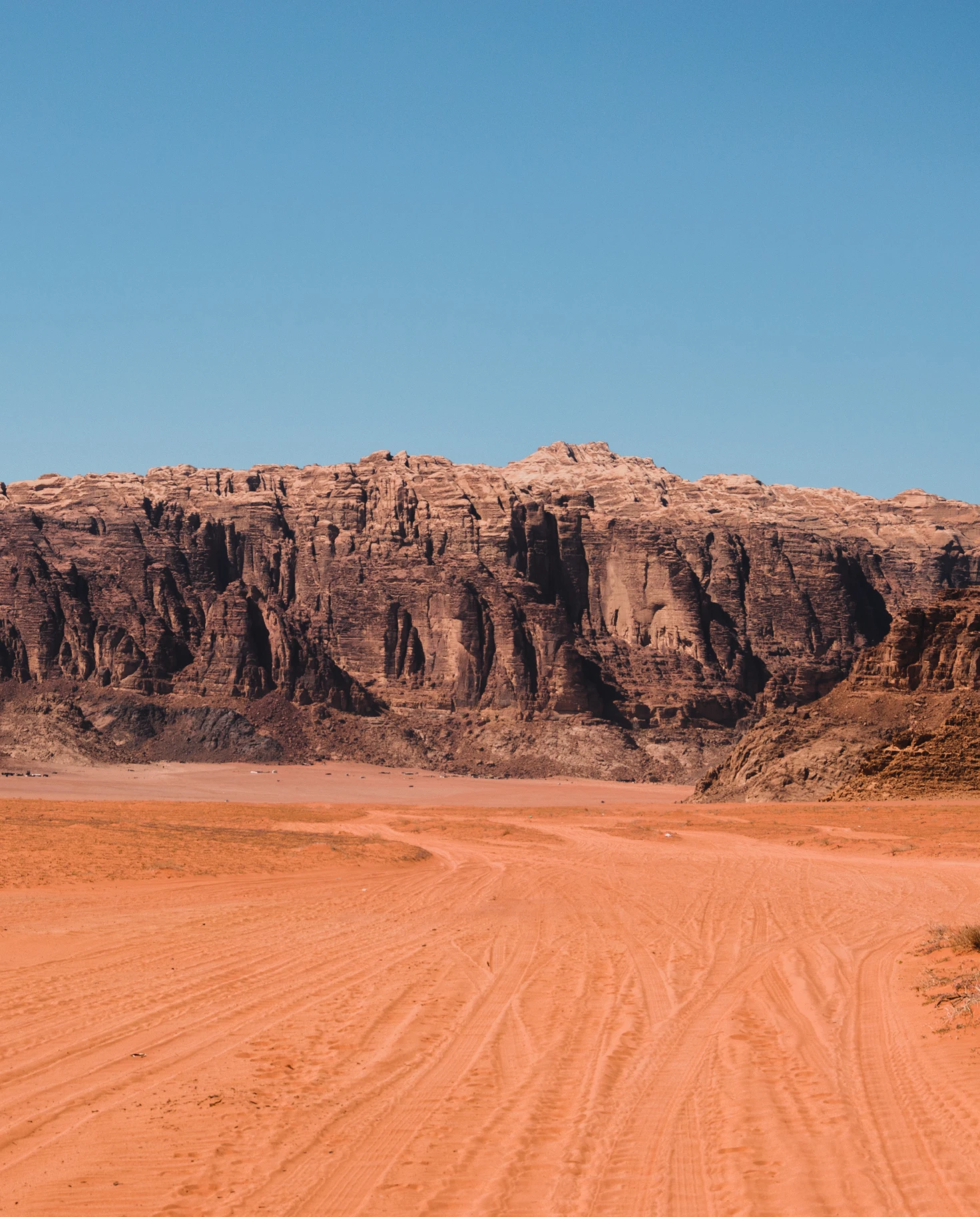 A visit to Jordan with red dirt roads and dark brown and red rock structures against a blue sky.