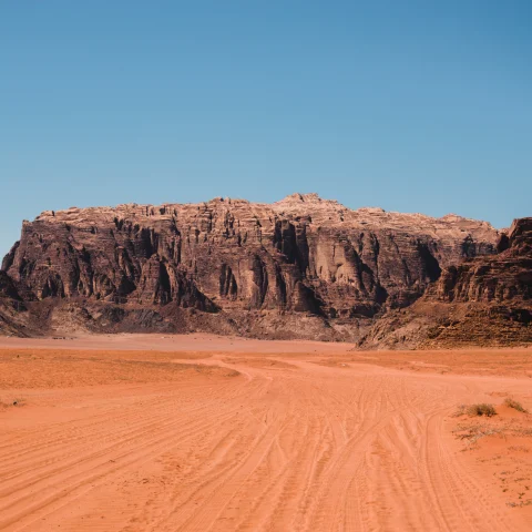 A visit to Jordan with red dirt roads and dark brown and red rock structures against a blue sky.