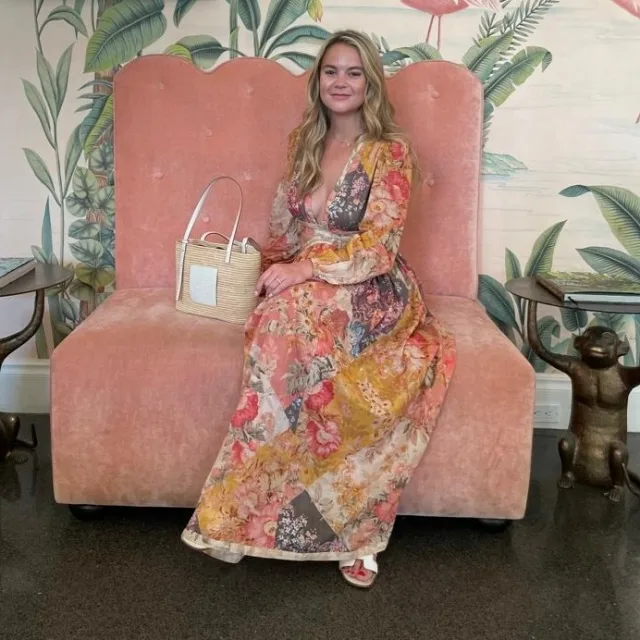 Travel Advisor Natalie Williams wears floral dress and lounges on coral colored couch