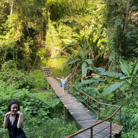 Two women posing on a path surrounded by lush and green plants and trees. 