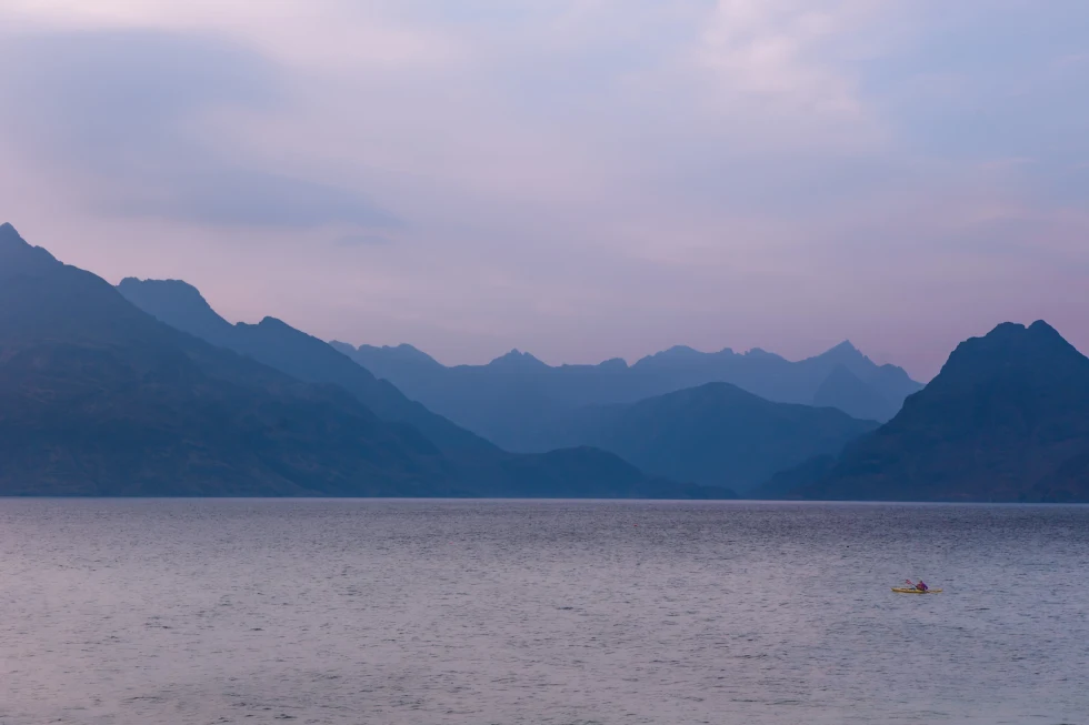 person kayaking in a body of water next to mountains