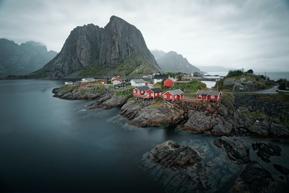 Body of water next to mountain and red buildings with cloudy skies