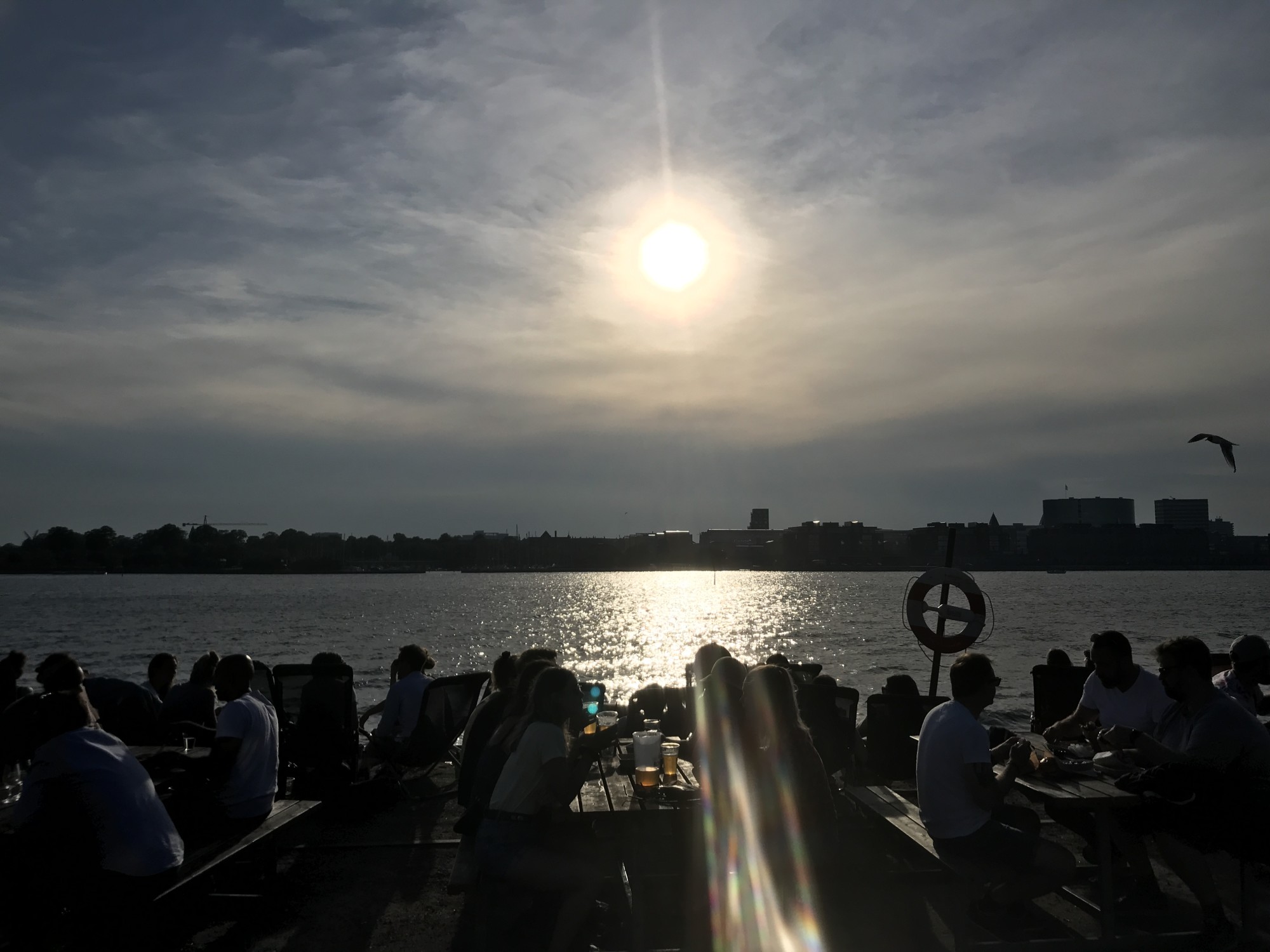 silhouettes of diners at a waterfront restaurant with sunset