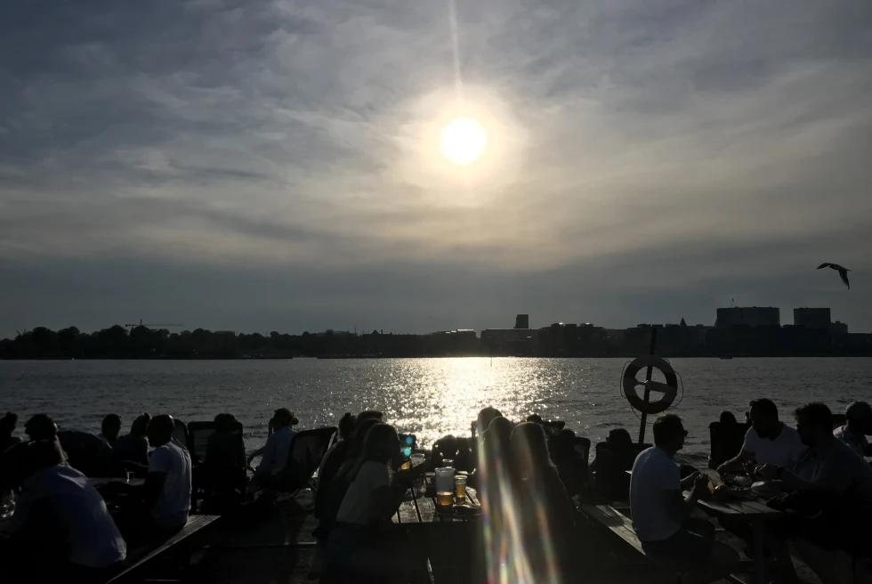 silhouettes of diners at a waterfront restaurant with sunset