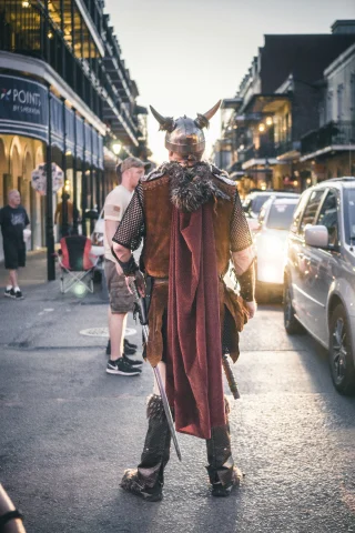 A picture of a man wearing a costume, standing in the middle of the road during daytime.